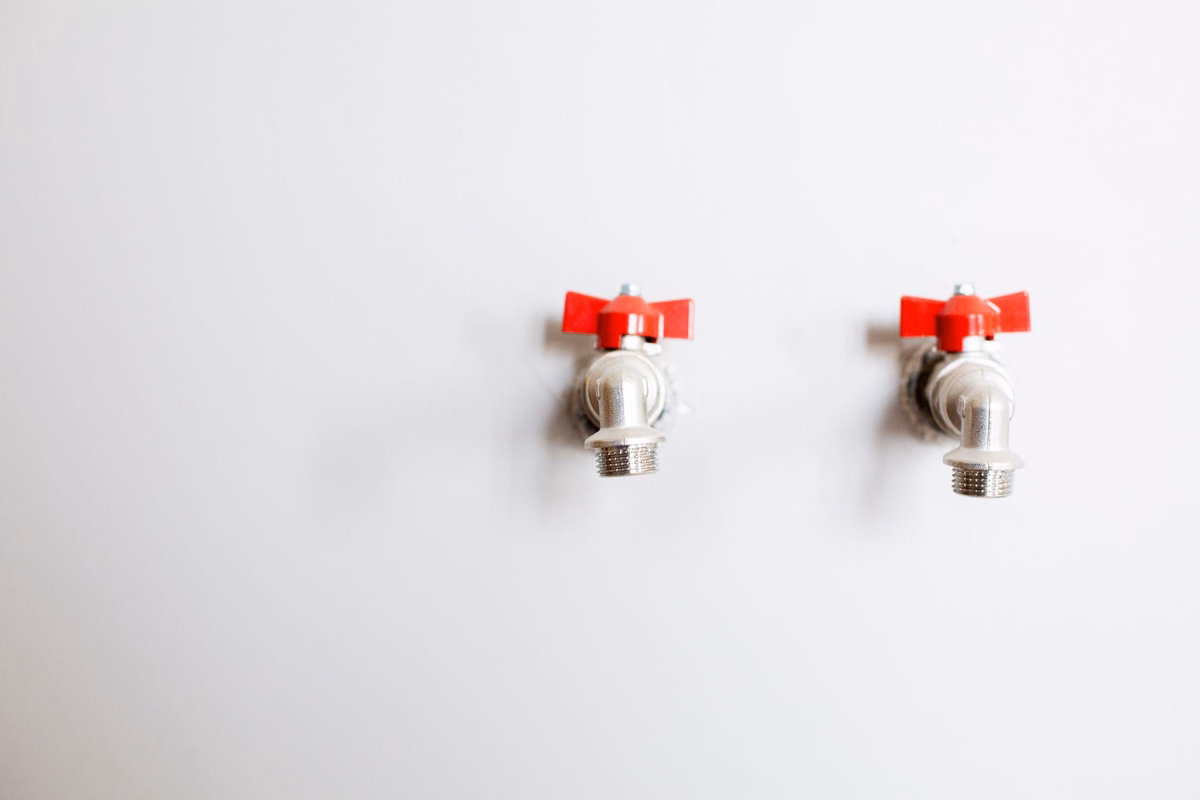 Two shutoff valves with red handles mounted on a clean white wall