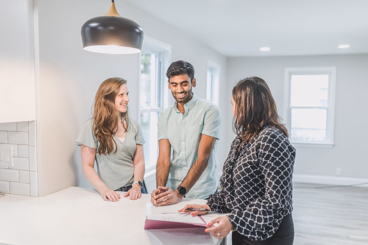 Real estate agent going over paperwork with a couple at a kitchen counter in a bright, empty home
