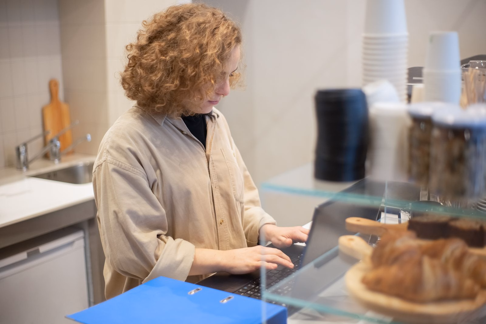 Cafe owner working on a laptop behind the counter next to a display of pastries
